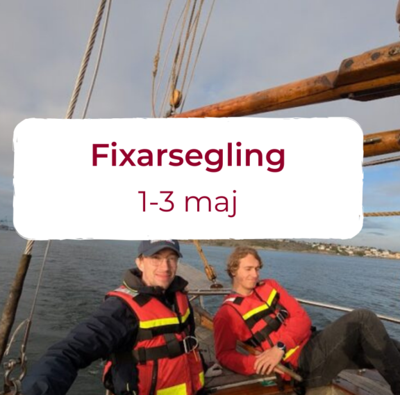 Två personer i flytvästar sitter på en segelbåt med vatten och en kustlinje i bakgrunden. Texten 