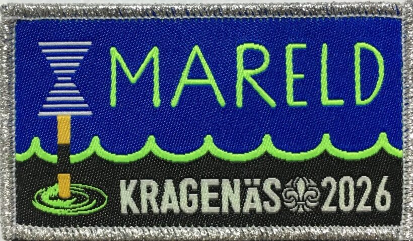 Tygmärke med texten "MARELD" i grönt på en blå bakgrund ovanför vågformer. En fyr med ljusstrålar syns till vänster, och nedanför står texten "KRAGENÄS 2026" i vitt tillsammans med en scoutlilja.