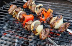 Grillspett med köttbitar, lök och paprika tillagas över glödande kol på en grill.
