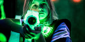 En person håller i en lasergevär med grönt ljus i en mörk miljö med neonbelysning.