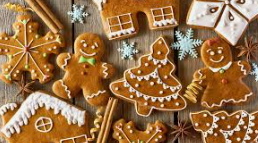 Pepparkakor dekorerade med glasyr i olika former, inklusive granar, hus, snögubbar och stjärnor, omgivna av kanelstänger och anis på en träyta.