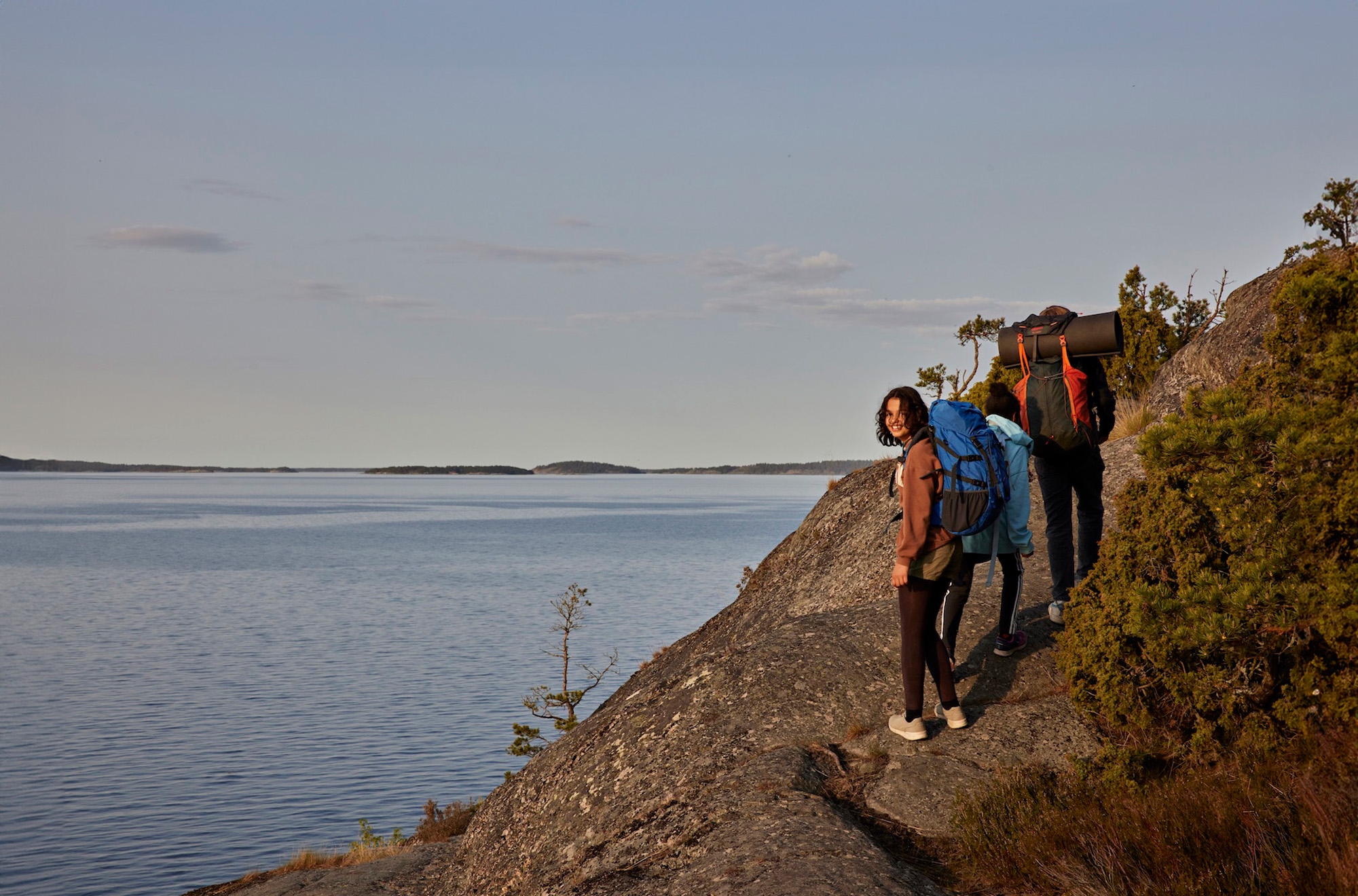 Två scouter med ryggsäckar vandrar på ett par klippor vid havet.
